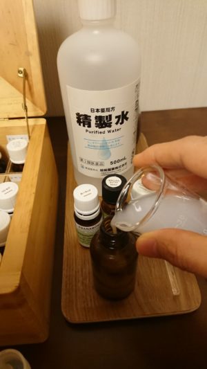 ビーカーから遮光瓶へ精油と精製水を乳化させたアロマ化粧水を丁寧に注いでいる様子。