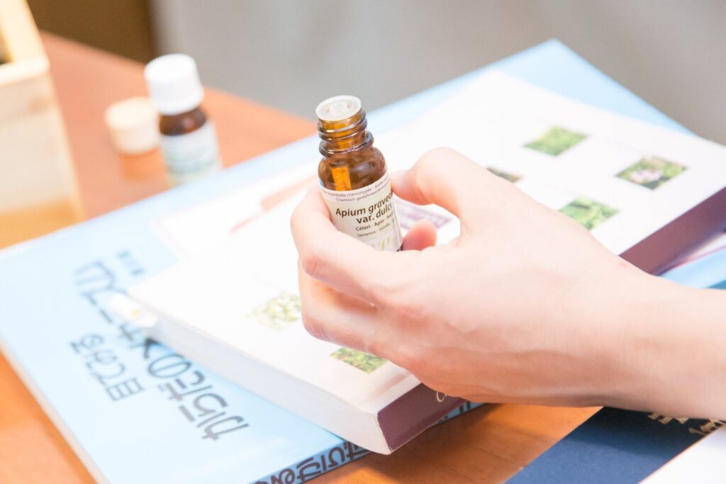 講座で使用す精油の瓶を手に持ちふたを開けた様子とアロマアドバイザーテキスト。実践的に学ぶアロマの現場をイメージさせる写真。