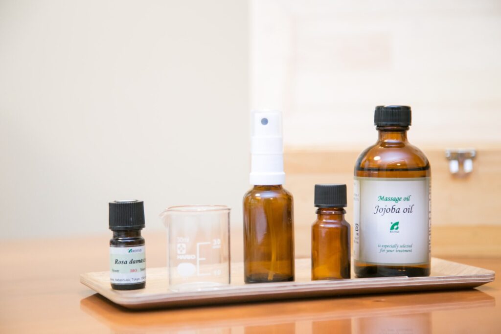 木のトレーに並べられた精油とジョホバオイル、ガラスビーカーとスプレーボトルの教材一式