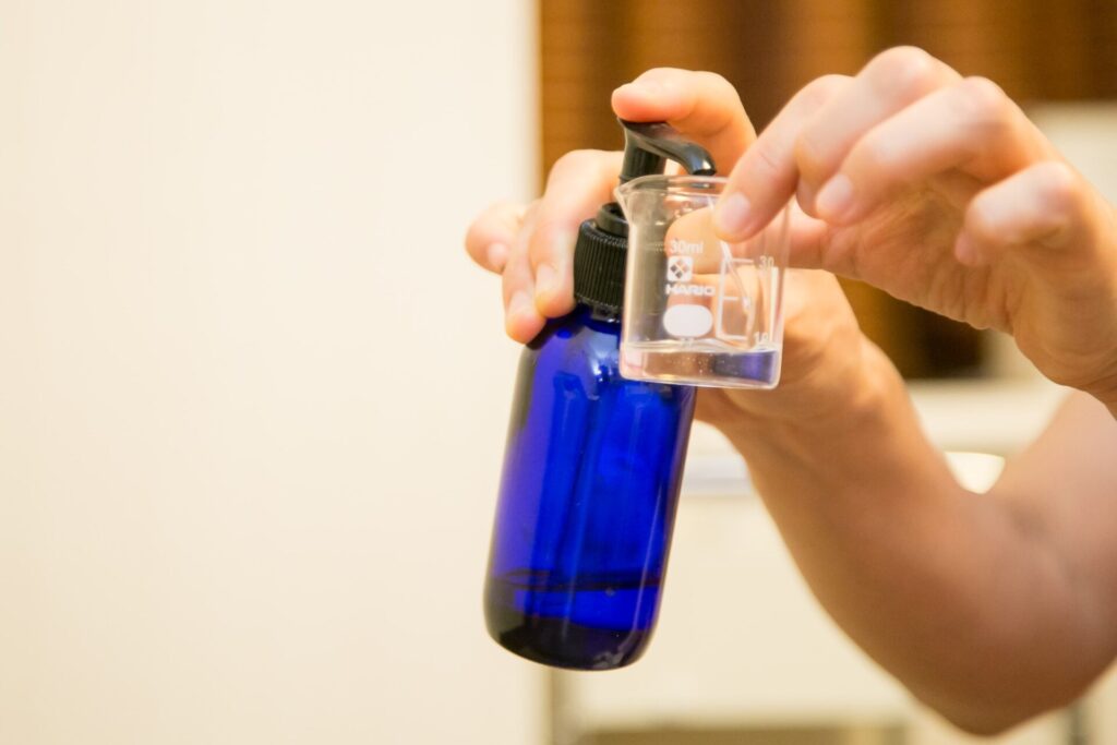 青色のボトルからビーカーに液体を計量している手元の写真