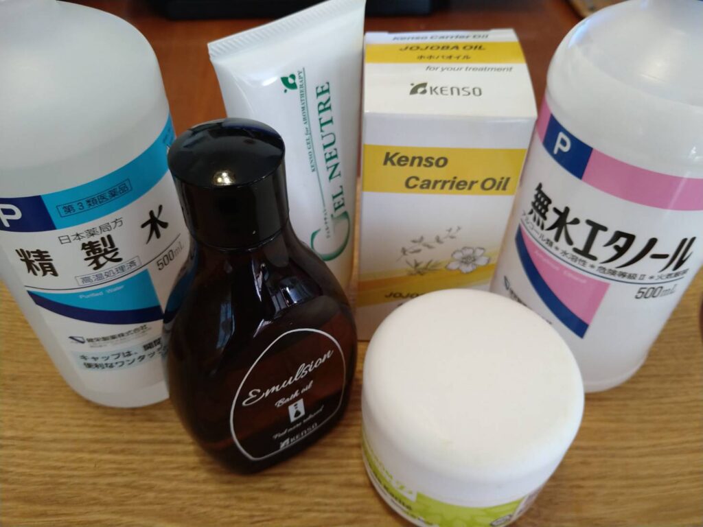 精製水、無水エタノール、ホホバ油、乳化剤ジェルなど、アロマテラピーで精油を希釈するための基剤をまとめて並べた写真。