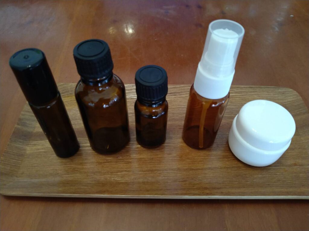 ロールオン容器、遮光ガラス瓶、スプレー容器、クリーム用ジャーなど、アロマクラフトに使用する保存容器を並べた写真。