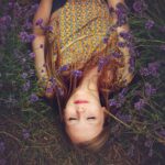 ラベンダー畑で目を閉じて横たわる女性の写真｜自然の香りに包まれるリラックスイメージ
