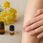 ヘリクリサムの花と精油瓶、ひざの傷にそっと触れる手元の応急ケアシーン