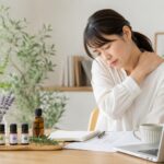 デスクワークによる肩こりに悩む女性が首に手を当て、精油を活用したメディカルアロマケアをイメージした画像